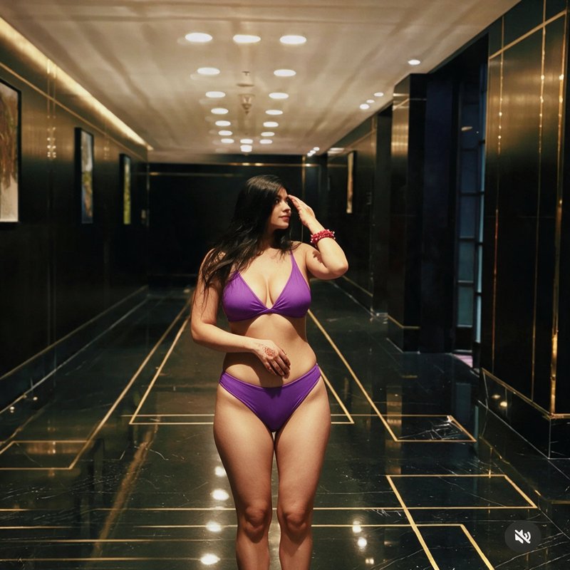 Confident woman in a purple bikini poses in a luxurious polished black and gold hotel hallway