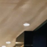 Low angle blurry view of warm wood grain ceiling with recessed downlights next to dark tinted win...