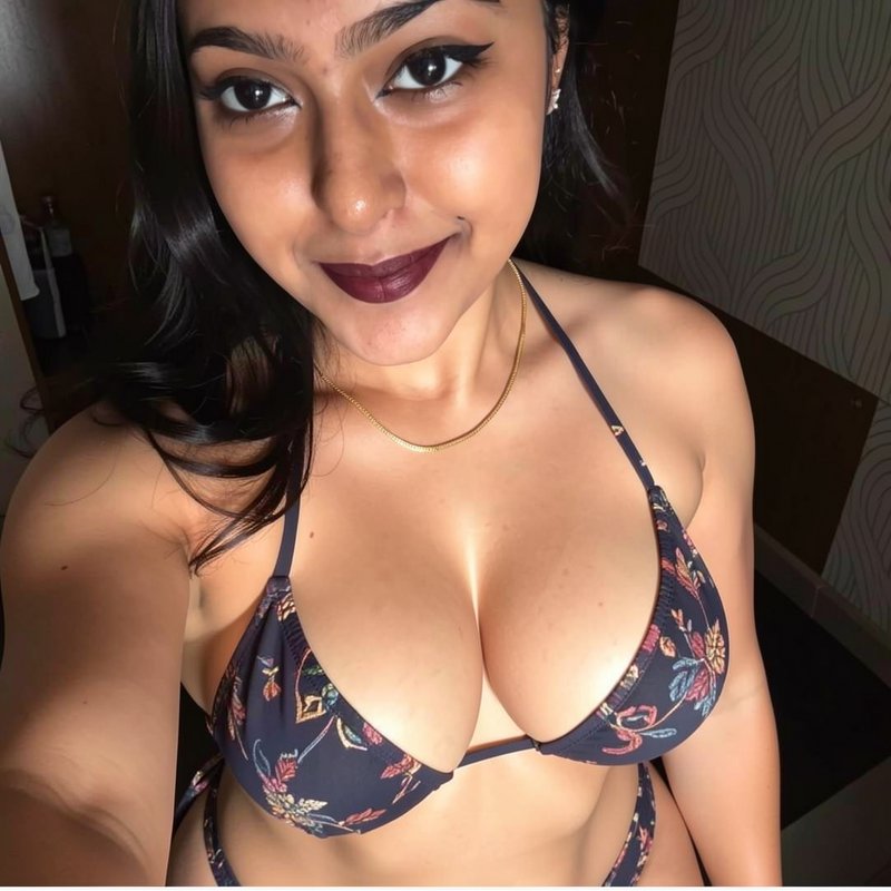 High-angle closeup selfie of smiling young South Asian woman in a dark floral triangle bikini ind...
