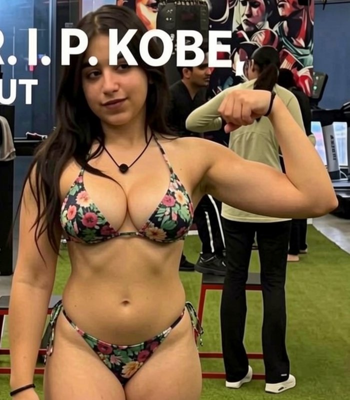Young fit woman in a floral bikini flexes her bicep in an indoor gym, with "R.I.P. KOBE" text ove...