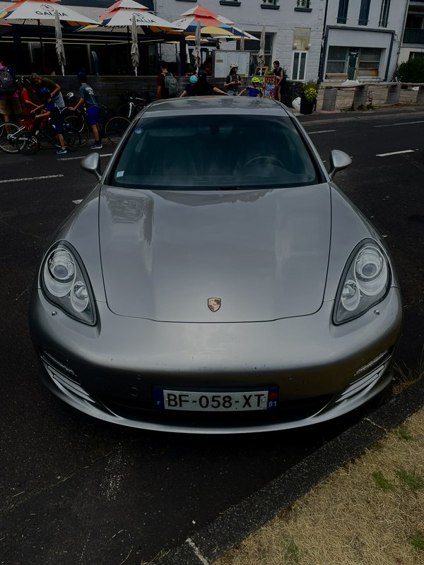 Front facing view of a glossy silver Porsche Panamera parked curbside on a paved French town street