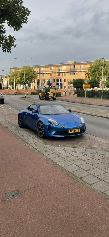 Bright blue Alpine A110 sports car parked on a curb at a Dutch residential street intersection un...