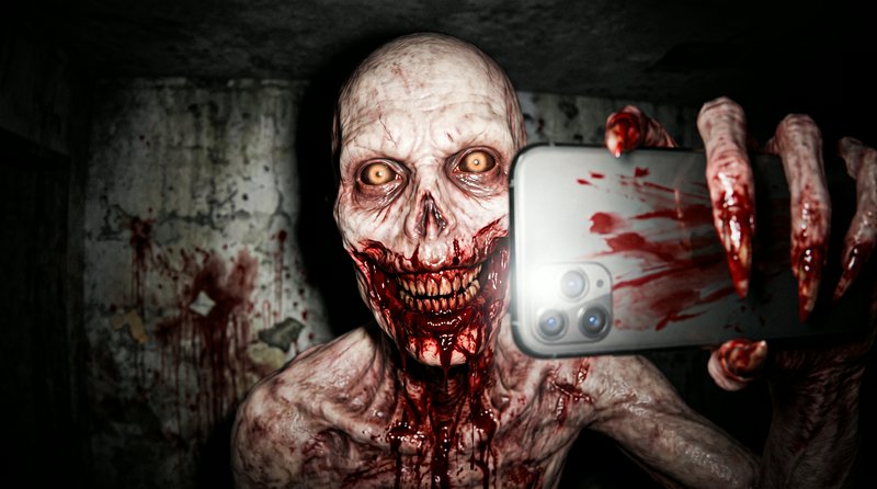 Grotesque blood-covered emaciated horror monster grins while holding a blood-smeared smartphone taking a selfie in a