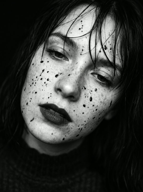 Close-up black and white portrait of a woman with wet hair, dark ink splatters on her face, and a...