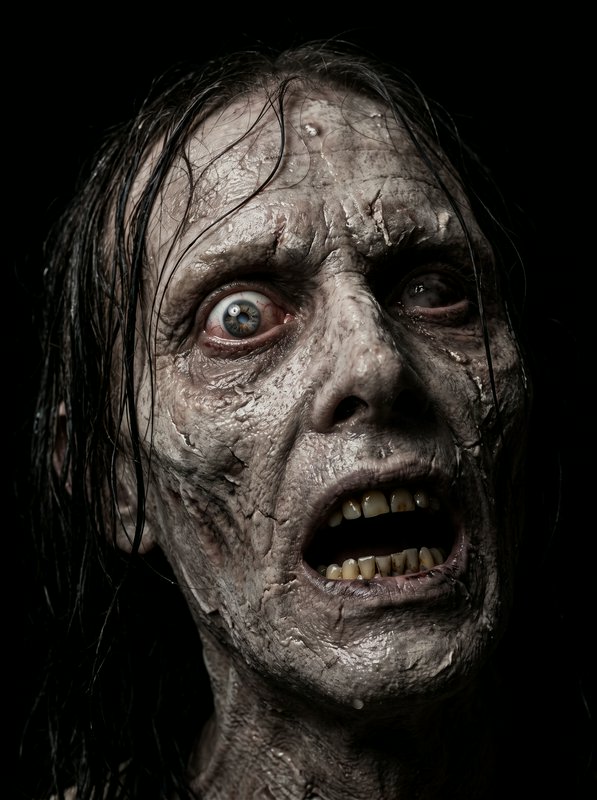 Close-up portrait of a decayed undead zombie with wide staring eyes against a black background