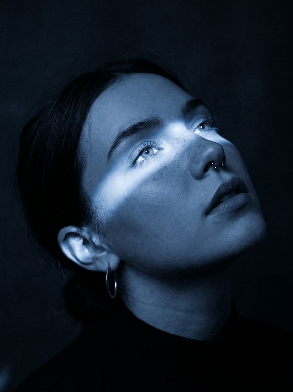 Moody blue portrait of a freckled woman gazing upward as a light streak crosses her face