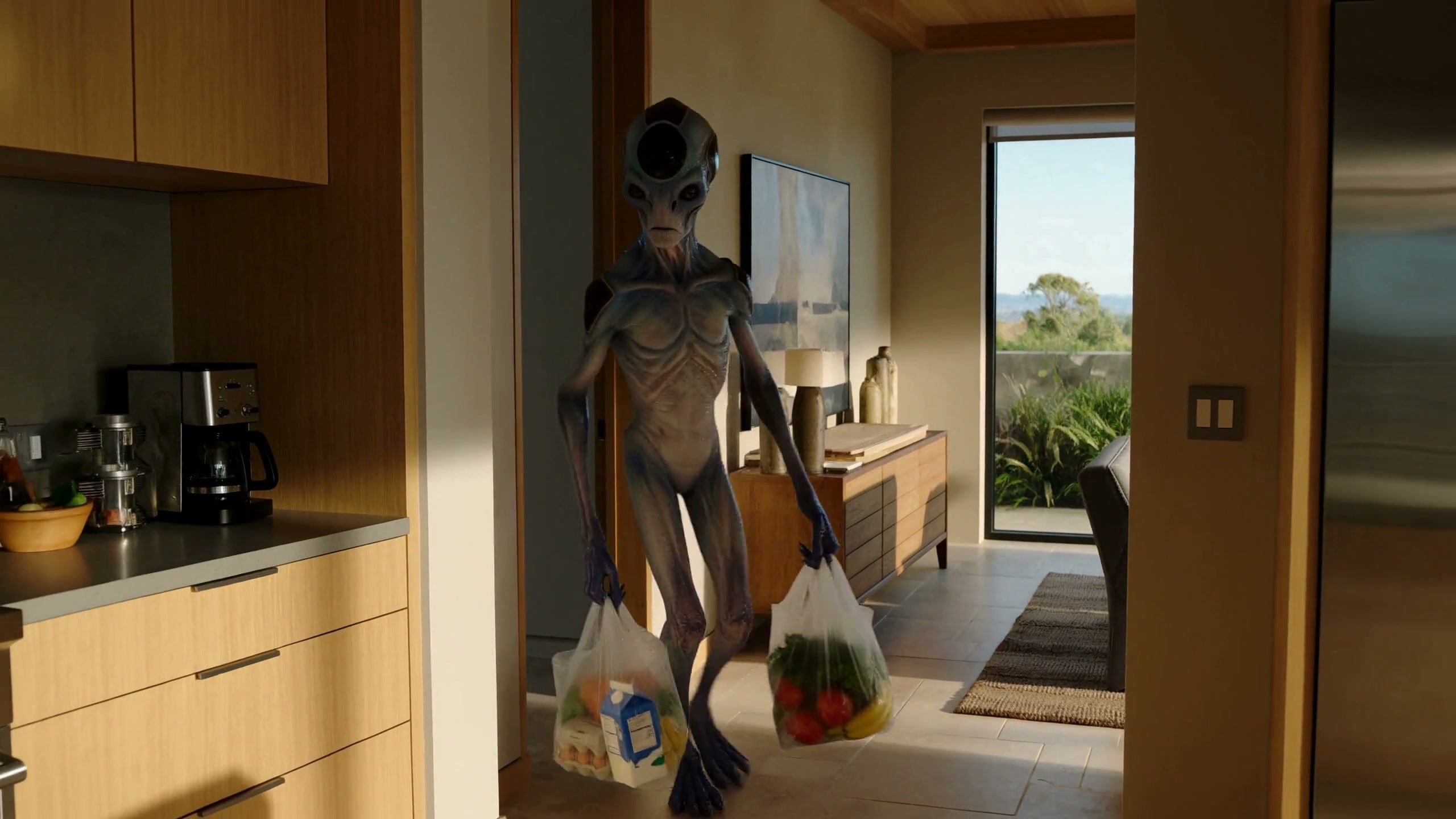 Classic grey alien carrying full grocery bags walks through a sunlit modern home entryway
