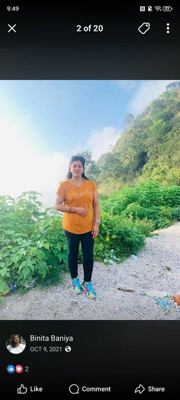 Casual portrait of a woman in an orange shirt standing on a gravel mountain trail beside lush gre...