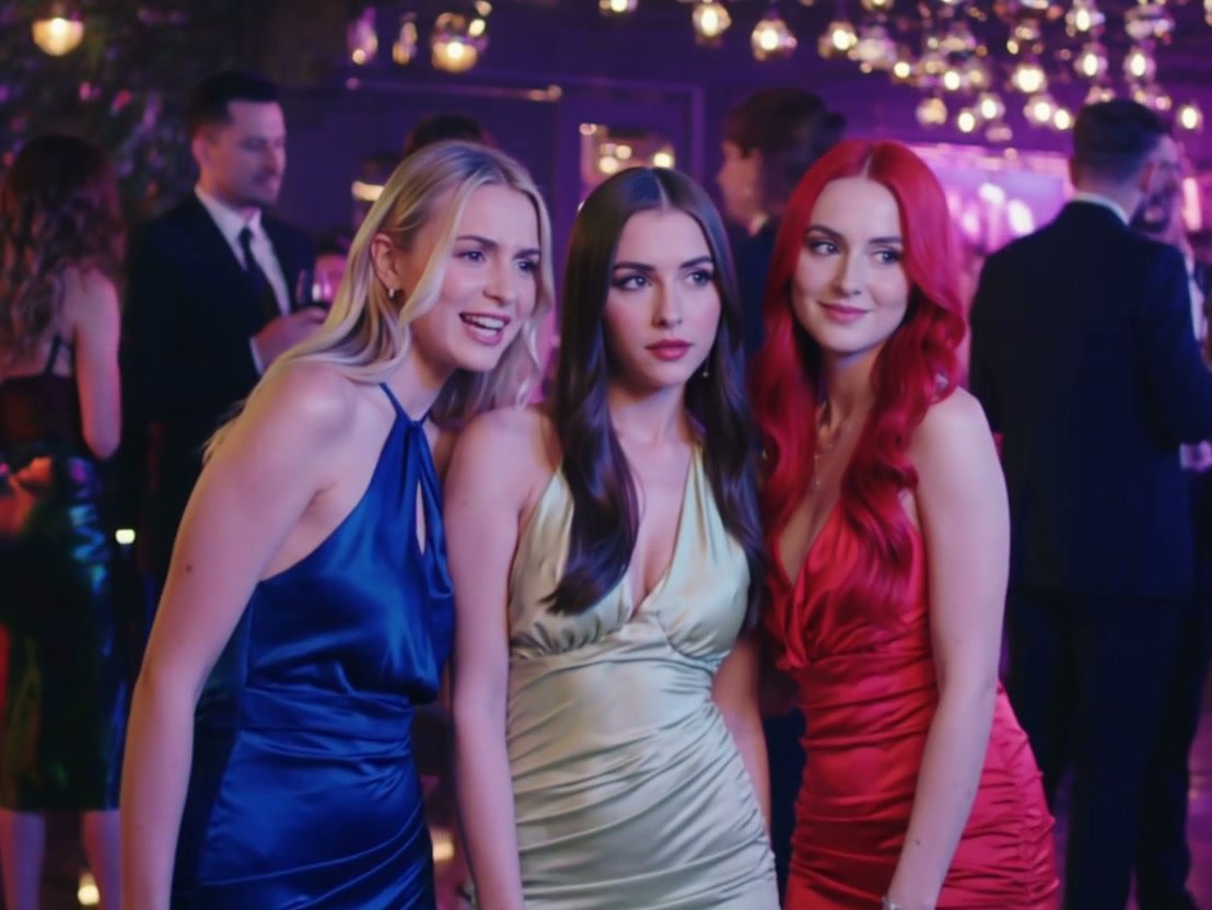 Three stylish women in colorful evening gowns posing at a nightclub party.