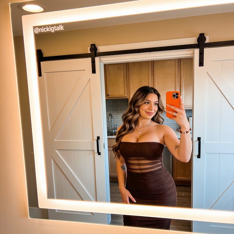 Smiling woman in a sheer panel brown strapless dress takes a selfie in a large illuminated LED va...