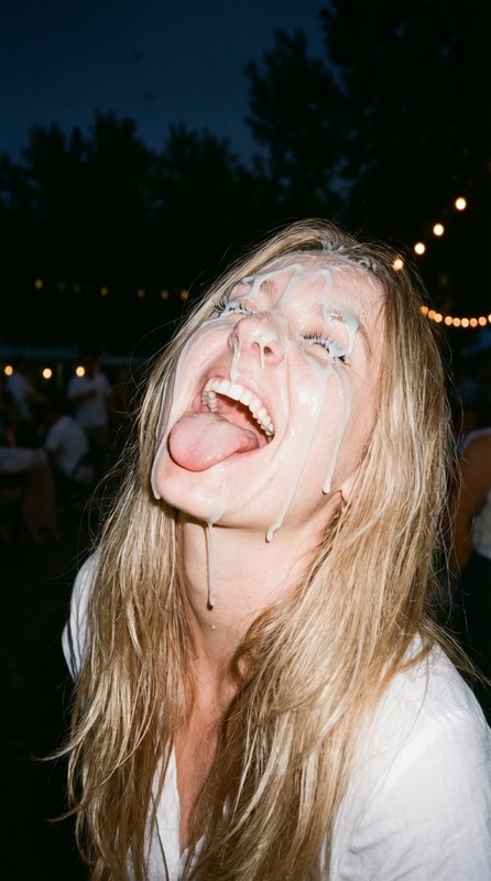 Candid shot of laughing blonde woman with dripping white cream on her face sticking her tongue ou...