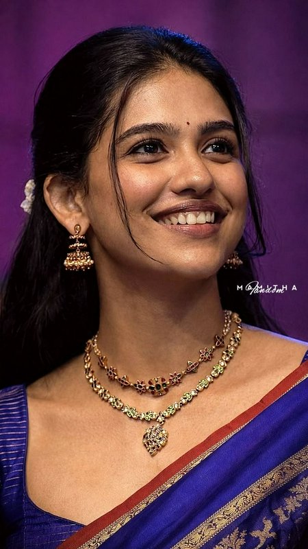 Close-up portrait of smiling young South Indian woman in blue silk saree with gold temple jewelry...