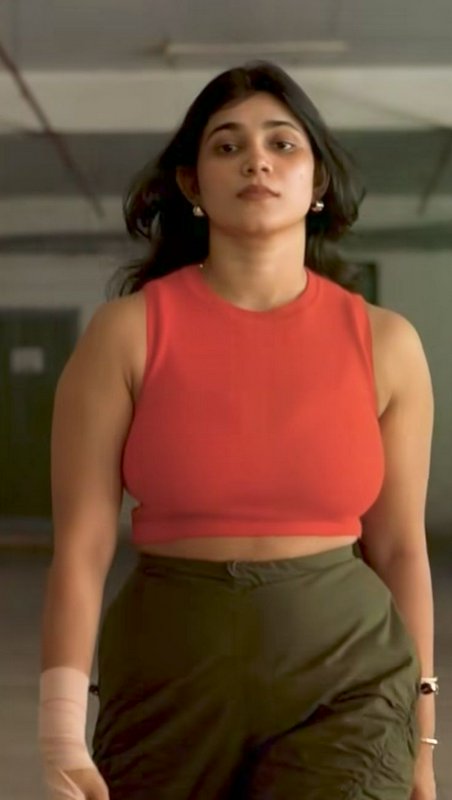Young South Asian woman in coral crop top and olive cargo pants walks toward the camera, with a b...