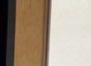 Close up of a vertical wooden door frame bordered by dark trim and a pale off-white interior wall