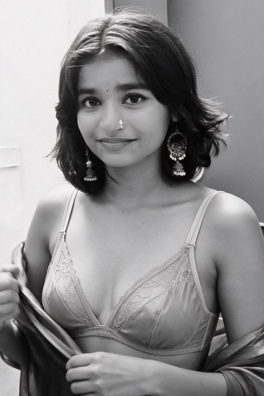 Black and white close-up portrait of young South Asian woman with short wavy hair, traditional je...