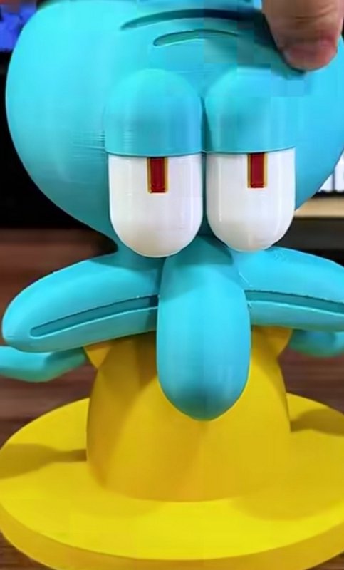 Close-up of a 3D printed Squidward Tentacles figurine, with a finger touching the top of his turq...