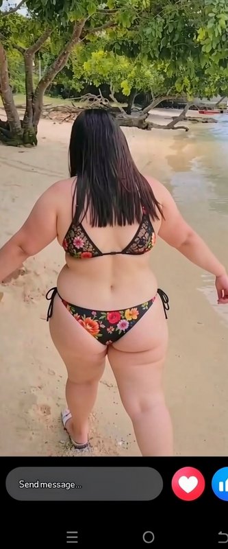 Rear view of a plus size woman in a floral bikini standing on a shaded tropical beach, social med...