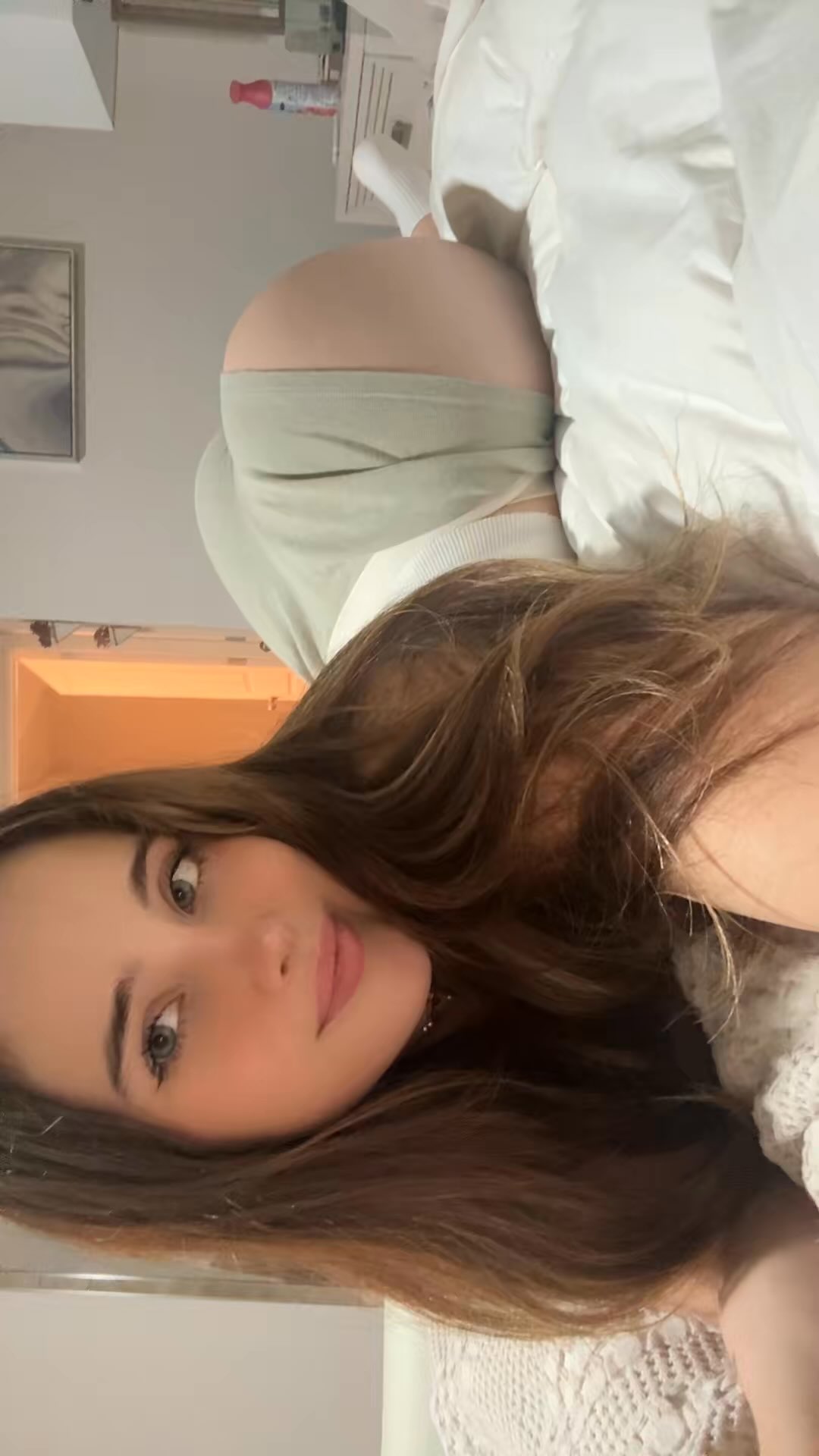 Young woman with long highlighted brown hair takes a casual selfie reclining on a bed