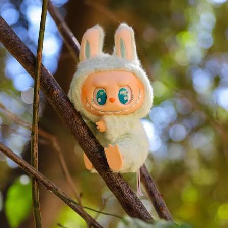 Fuzzy pastel mint Labubu plush collectible perched on tree branches against sunlit blurred forest...
