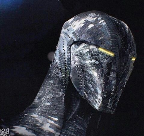 Close-up of a segmented silver alien Predator helmet with glowing yellow eye slits against a dark...