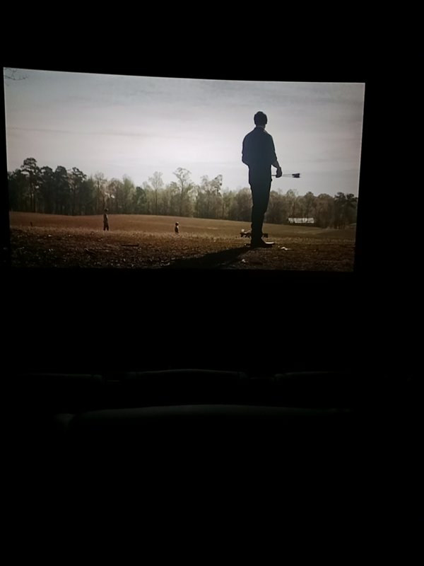 Silhouetted man holding a rifle stands in a sunlit rural field viewed on a home television screen