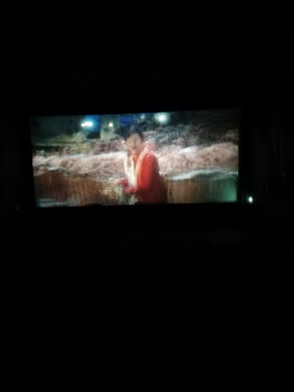 Wide cinema screen displaying a film scene of a person in red against rushing floodwaters