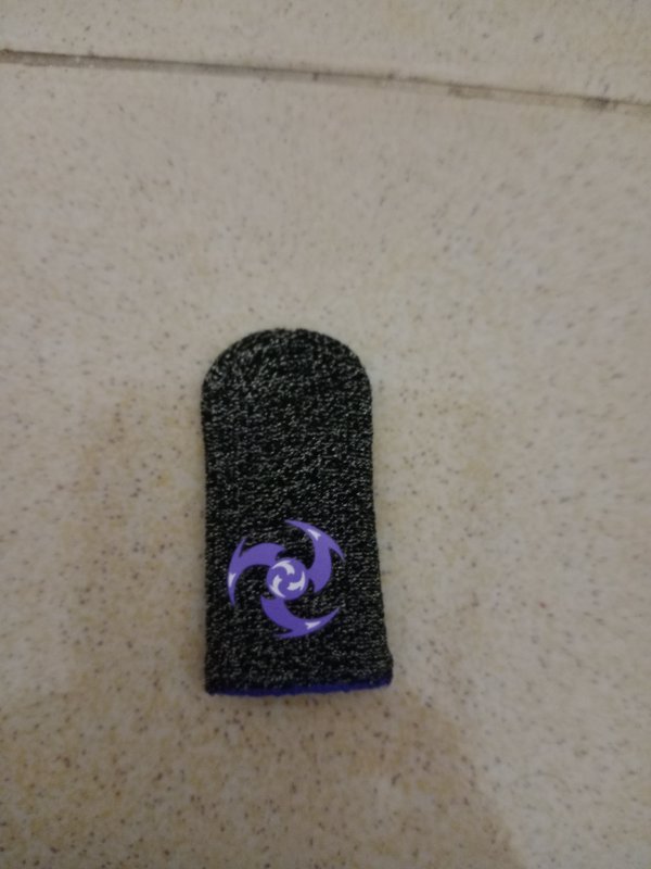 Black knit mobile gaming finger sleeve with purple swirl logo resting on a speckled beige tile su...