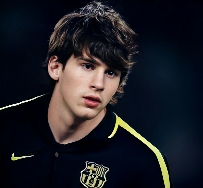 Close-up portrait of young Lionel Messi in a vintage FC Barcelona training jacket against a dark ...