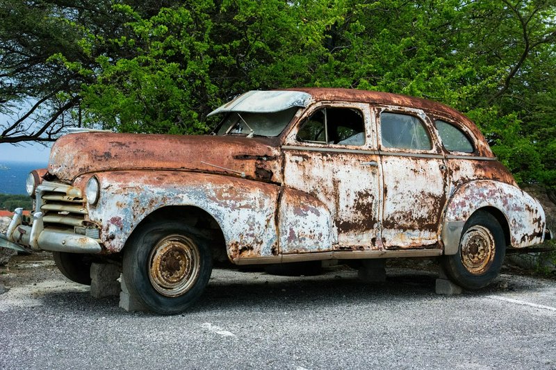 Heavily rusted abandoned 1940s vintage sedan propped on concrete blocks overlooking the ocean bes...