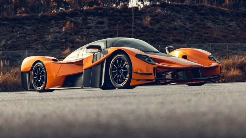Side profile view of glossy orange futuristic aerodynamic hypercar parked on asphalt road at gold...