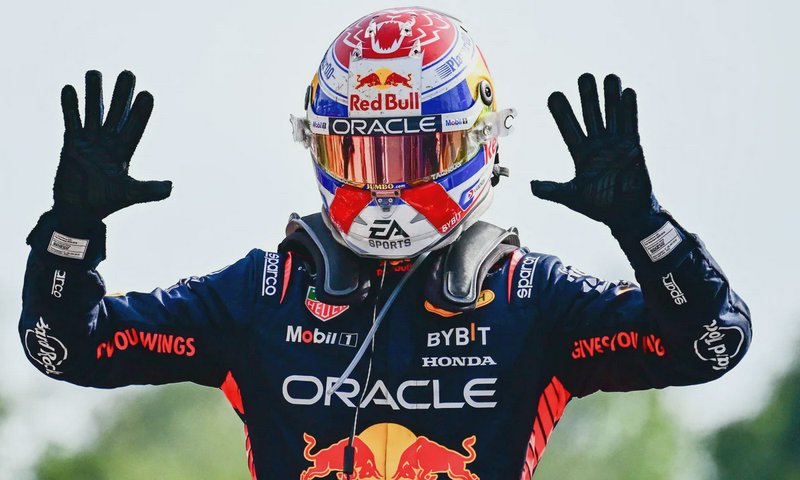 Oracle Red Bull F1 driver raises both black gloved hands in celebration, wearing a branded custom...