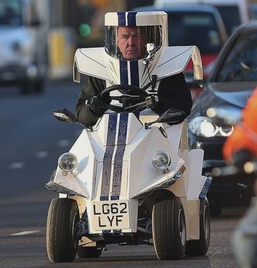 Jeremy Clarkson driving a tiny custom race-striped mobility car with matching integrated helmet o...