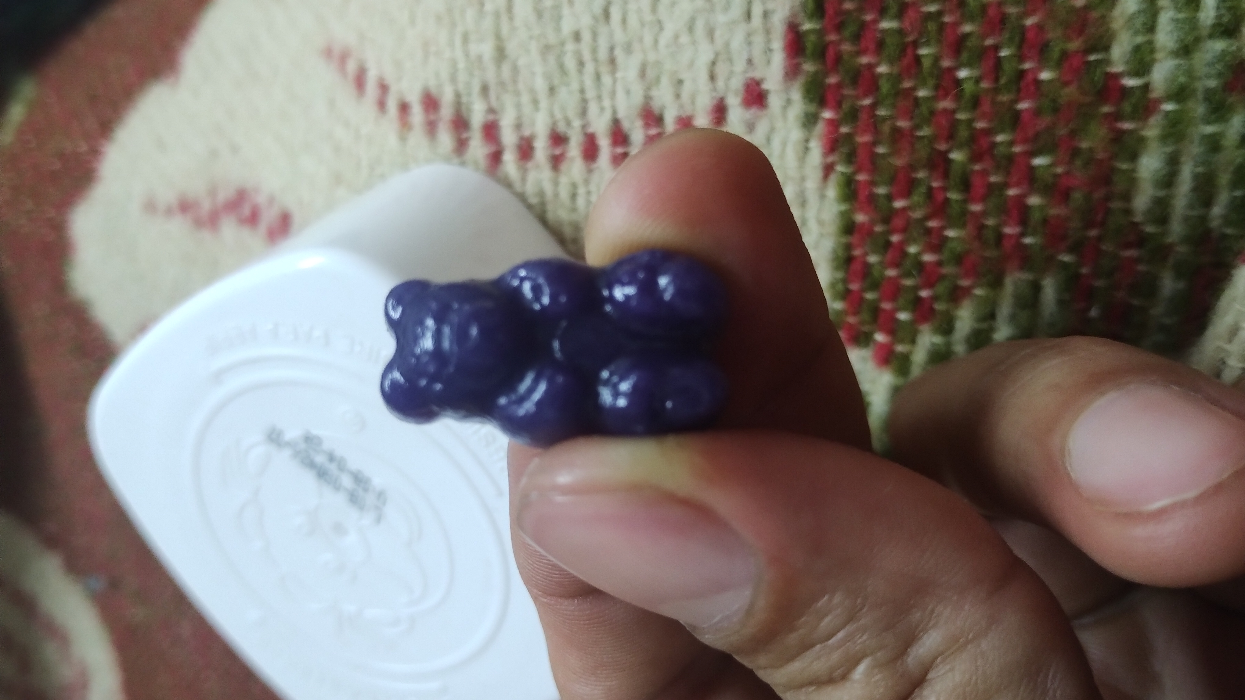 Person holding a glossy dark purple gummy bear between their fingertips above a candy mold