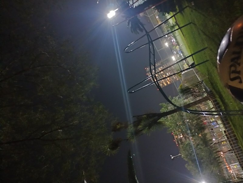Tilted night view of a lit neighborhood park, streetlight lens flare, partial Spalding basketball...