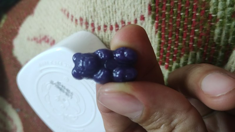 Person holding a glossy dark purple gummy bear between their fingertips above a candy mold