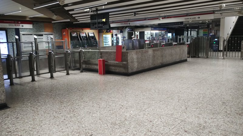 Empty underground subway station concourse with entry turnstiles, ticket vending machines, and ov...