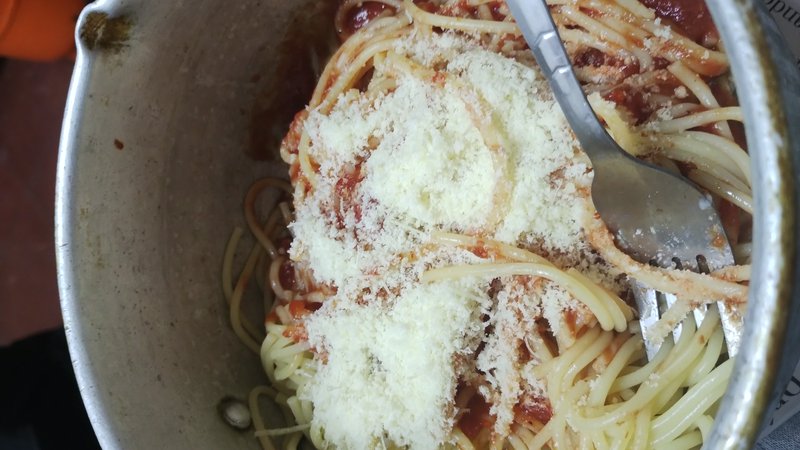 Top-down view of spaghetti with tomato sauce and grated cheese in a metal pot with a tucked-in me...