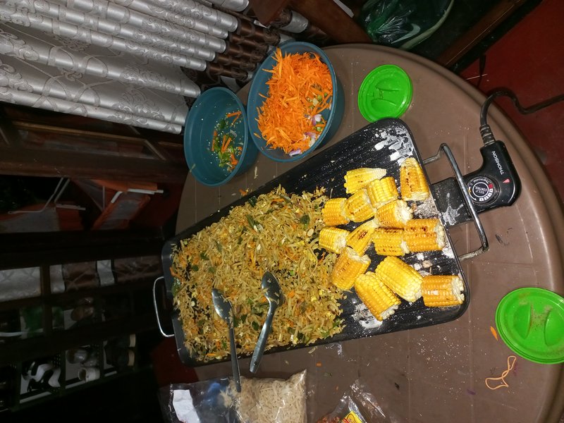 Top-down view of electric tabletop griddle with vegetable stir fry and grilled corn, prep bowls o...