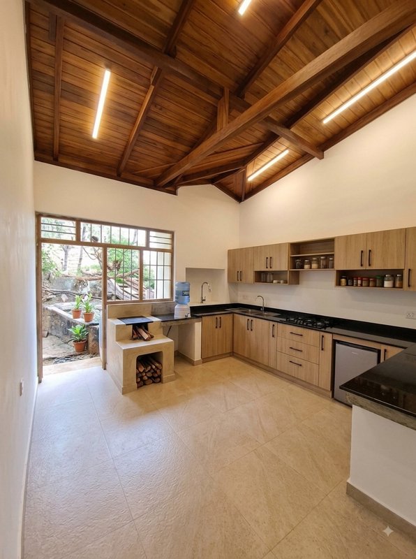Spacious rustic modern kitchen with vaulted exposed wood ceiling, light cabinetry, wood-fired coo...
