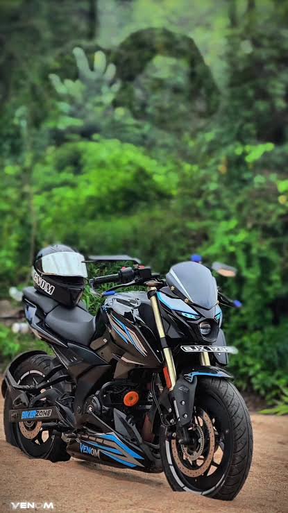 Custom black and blue naked sport motorcycle parked on a dirt path, helmet on seat, blurred lush ...