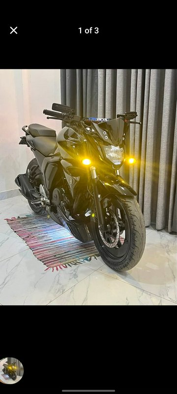 Glossy black naked street motorcycle with glowing yellow auxiliary lights parked indoors on a wov...