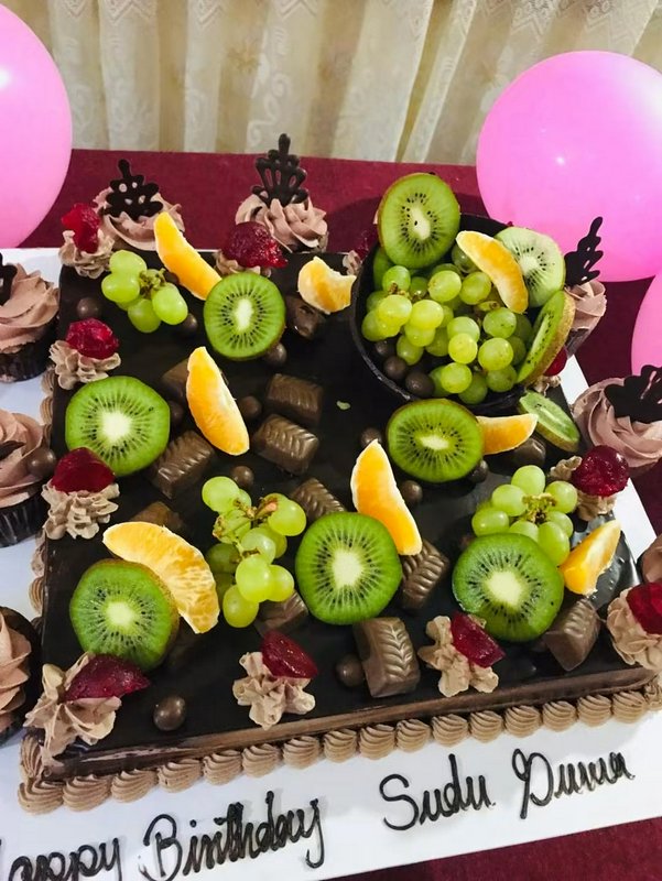 Oversized chocolate birthday cake piled high with fresh fruit, chocolates, and decorative party a...