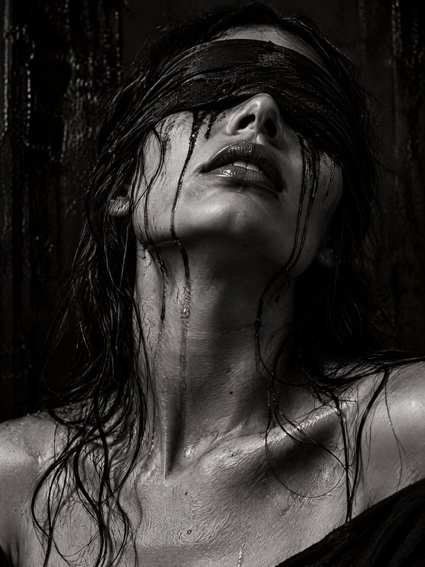 Blindfolded woman with wet glistening skin tilts her head back as dark liquid drips down her face