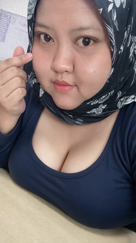 Close-up indoor selfie of a woman in a black floral hijab holding her hand gently next to her face
