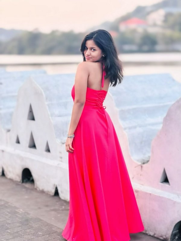 Young woman in bright fuchsia halter maxi dress looks over her shoulder on a waterfront terrace a...