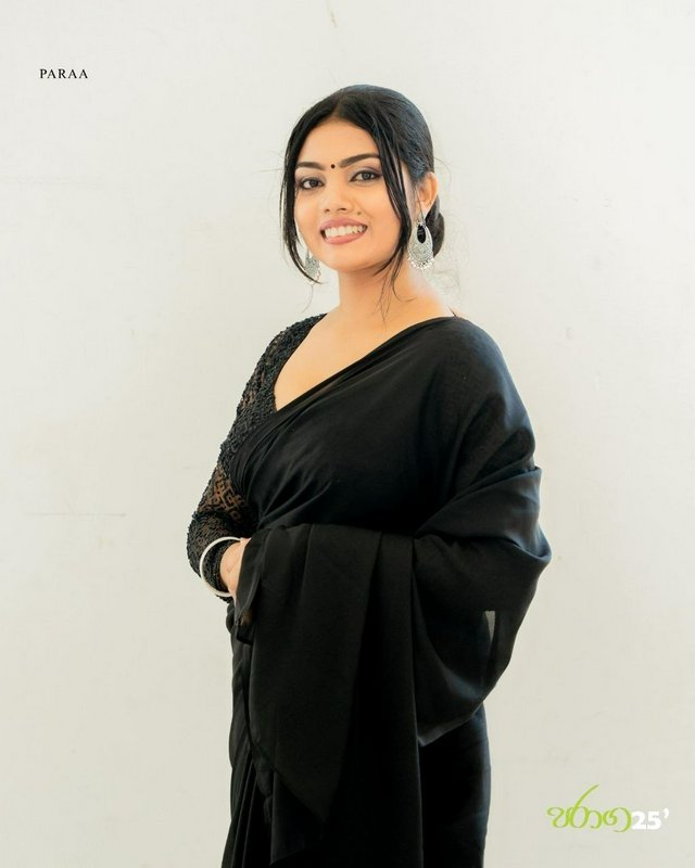 Smiling young South Asian woman in an elegant black satin saree poses against a plain light neutr...