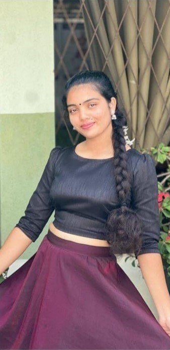 Young South Asian woman with a long side braid, smiling softly, wearing a black crop top and flow...