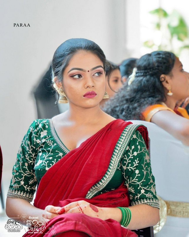 Young Sri Lankan woman in a red saree and green embroidered blouse seated at a formal cultural event