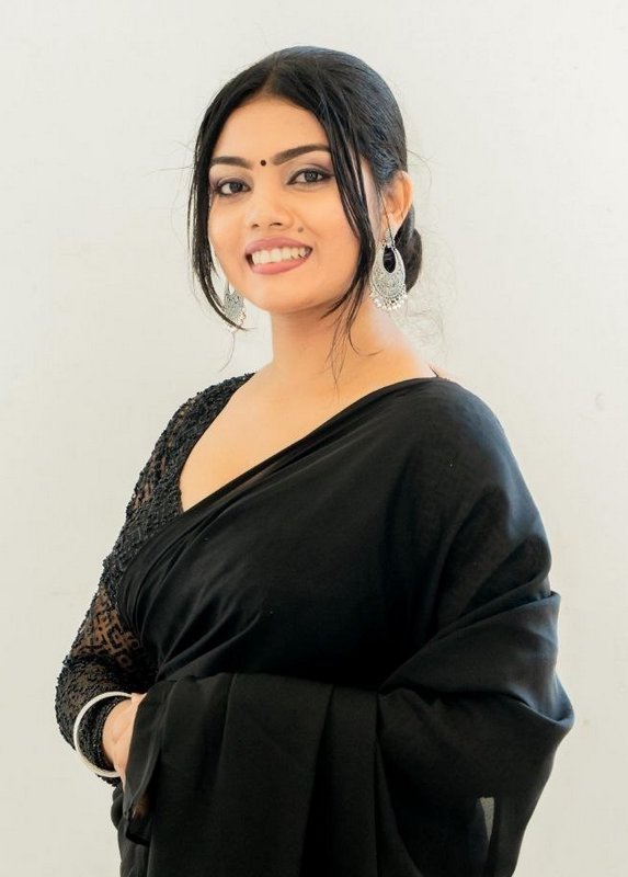 Smiling South Asian woman in a black saree poses against a plain light off-white wall