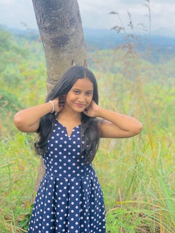 Young woman in navy polka dot dress smiles leaning against a tree on a misty green hilltop overlook